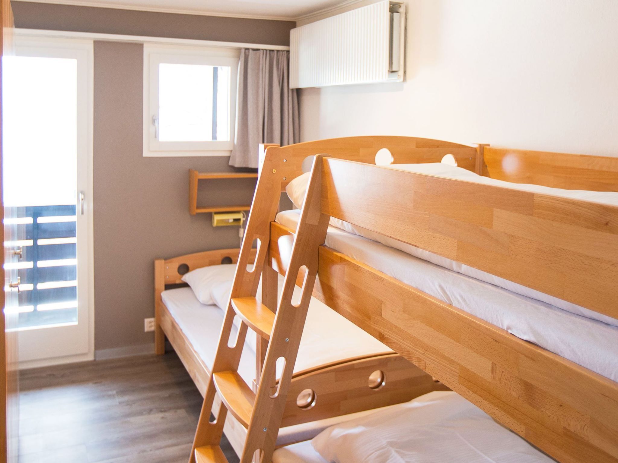 Ein Stockbett mit Holzbettgestell und weißer Bettwäsche in einem Zimmer mit Schiebetür und Fenster.