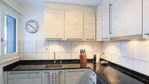 A modern kitchen with white cabinets, a black countertop, a stainless steel sink, and a clock on the wall. - Club Siesta Ferienwohnung/Studio, (Flumserberg Tannenheim), by Interhome (Flumserberg Tannenheim)