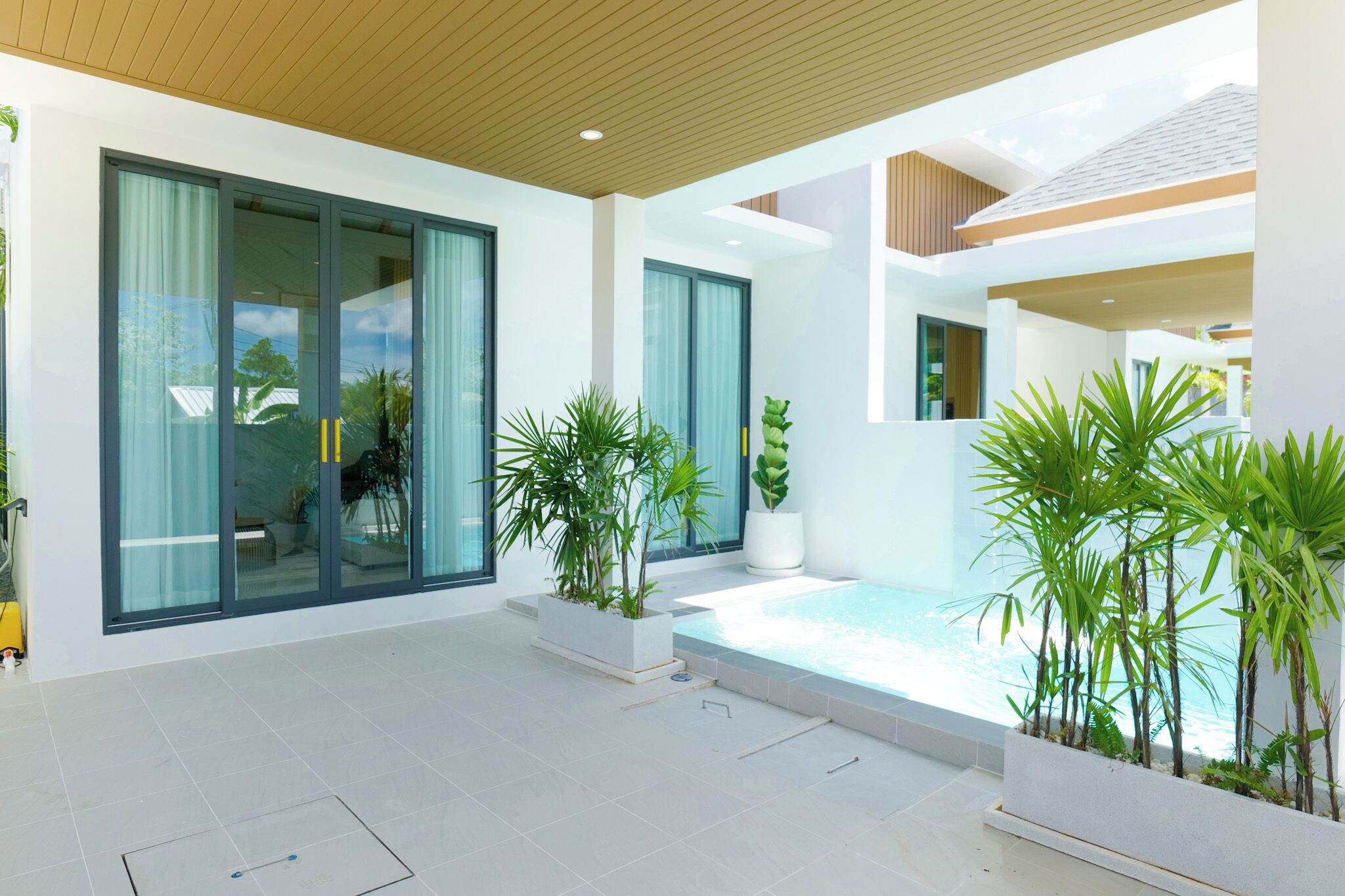 A modern house with large sliding glass doors, a swimming pool, and potted plants.