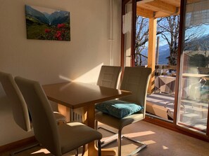 A dining area with a table and chairs, a window with a view of mountains, and a painting on the wall.