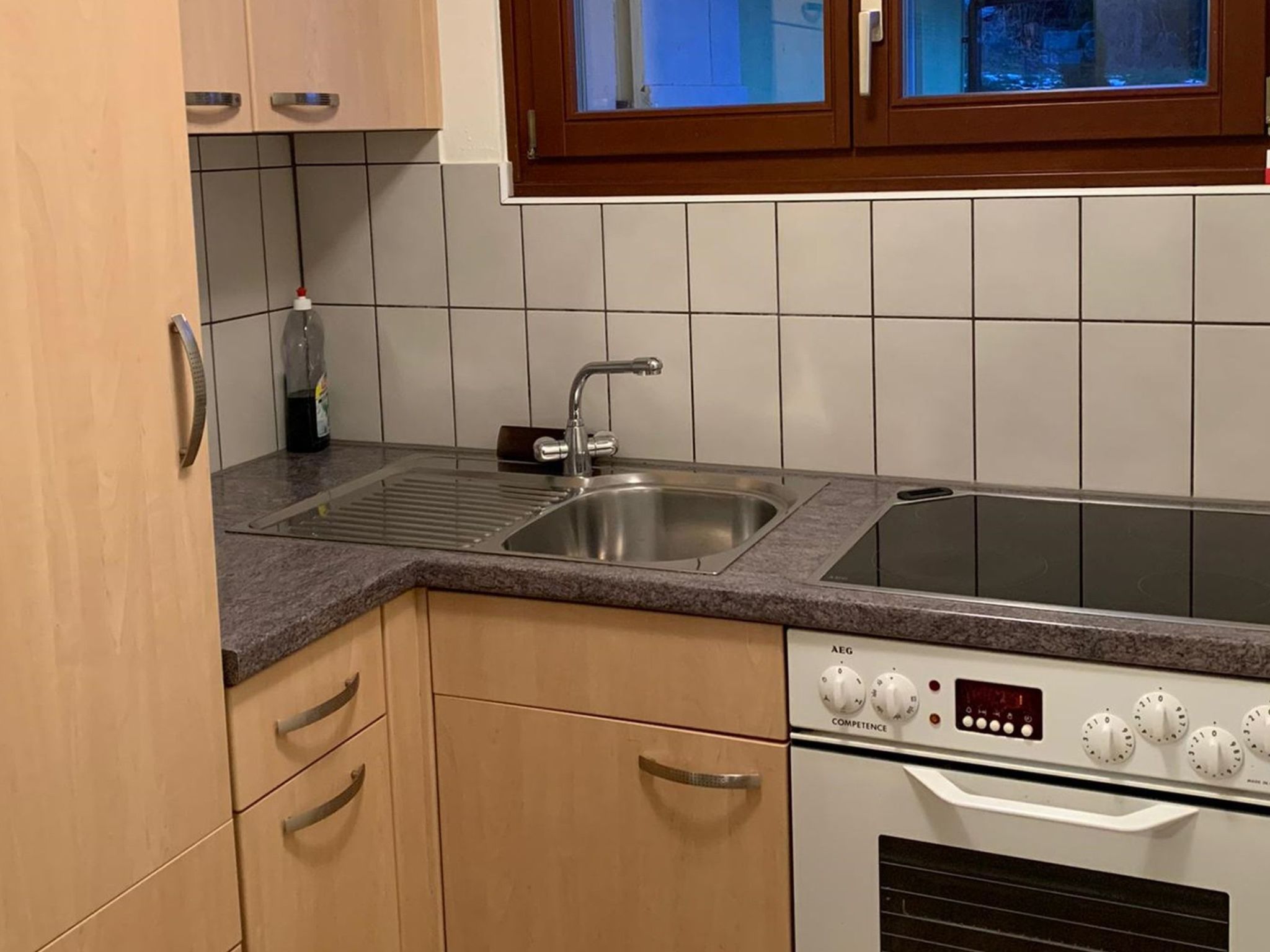 Eine Küche mit einer Edelstahl-Spüle, einem eingebauten Backofen und einem Fenster über der Spüle.