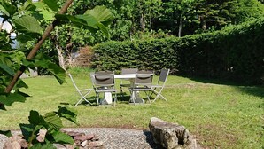 Un espace extérieur aménagé avec une table et des chaises, entouré d’une pelouse et d’une haie.