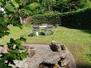 An outdoor seating area with a table and chairs, surrounded by a grassy lawn and a hedge. - Chalet Rehwiesli, (Flumserberg Tannenheim), by Interhome (Flumserberg Tannenheim)