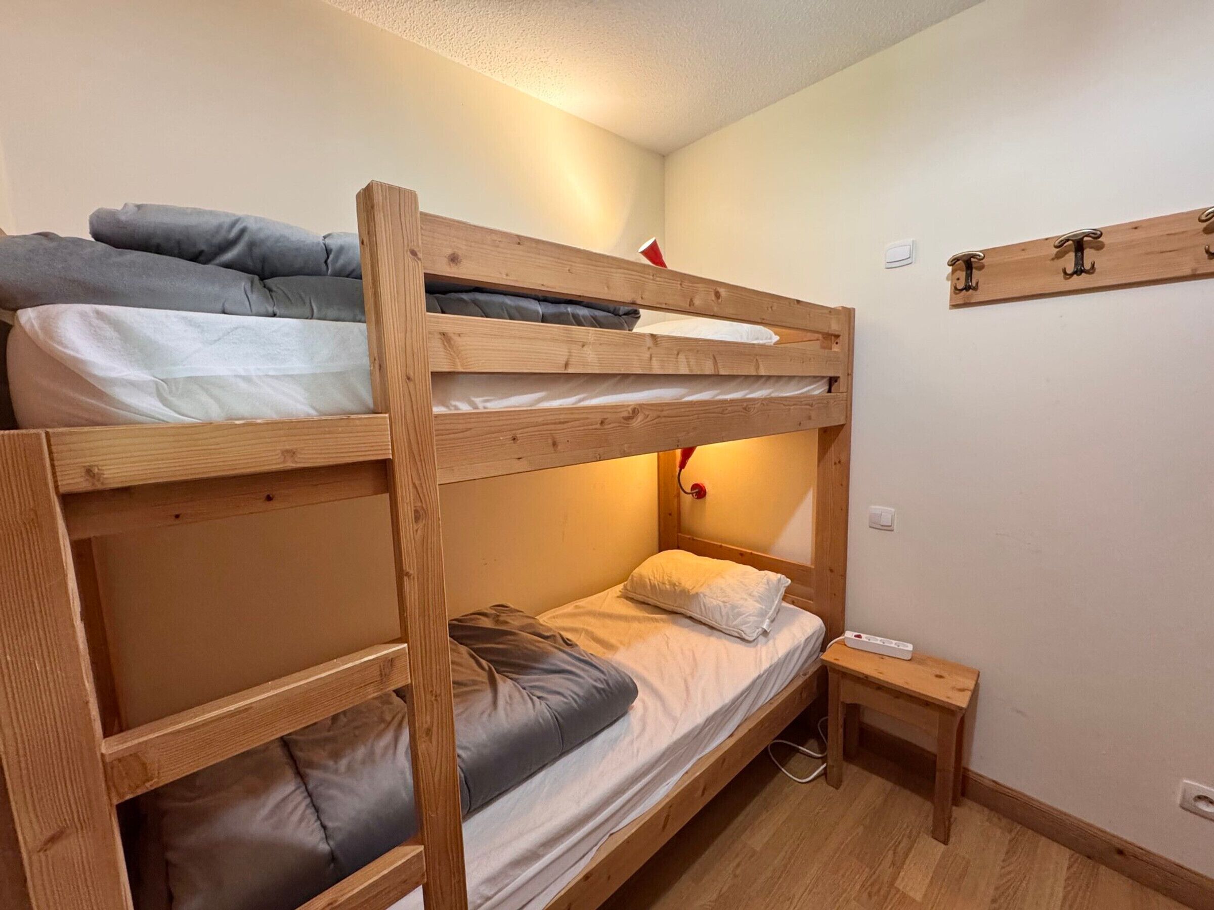 Une chambre avec un lit superposé, une petite table de chevet et une étagère fixée au mur.