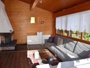 Een gezellige woonkamer met een open haard, een bank, een salontafel en een groot raam met gordijnen.