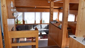 A wooden cabin interior with a sofa, a small table, and a view through the windows. - Chalet am Tobelbach, (Flumserberg Tannenheim), by Interhome (Flumserberg Tannenheim)