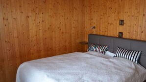 A bedroom with a wooden paneled wall, a bed with white bedding, and two pillows. - Chalet am Tobelbach, (Flumserberg Tannenheim), by Interhome (Flumserberg Tannenheim)