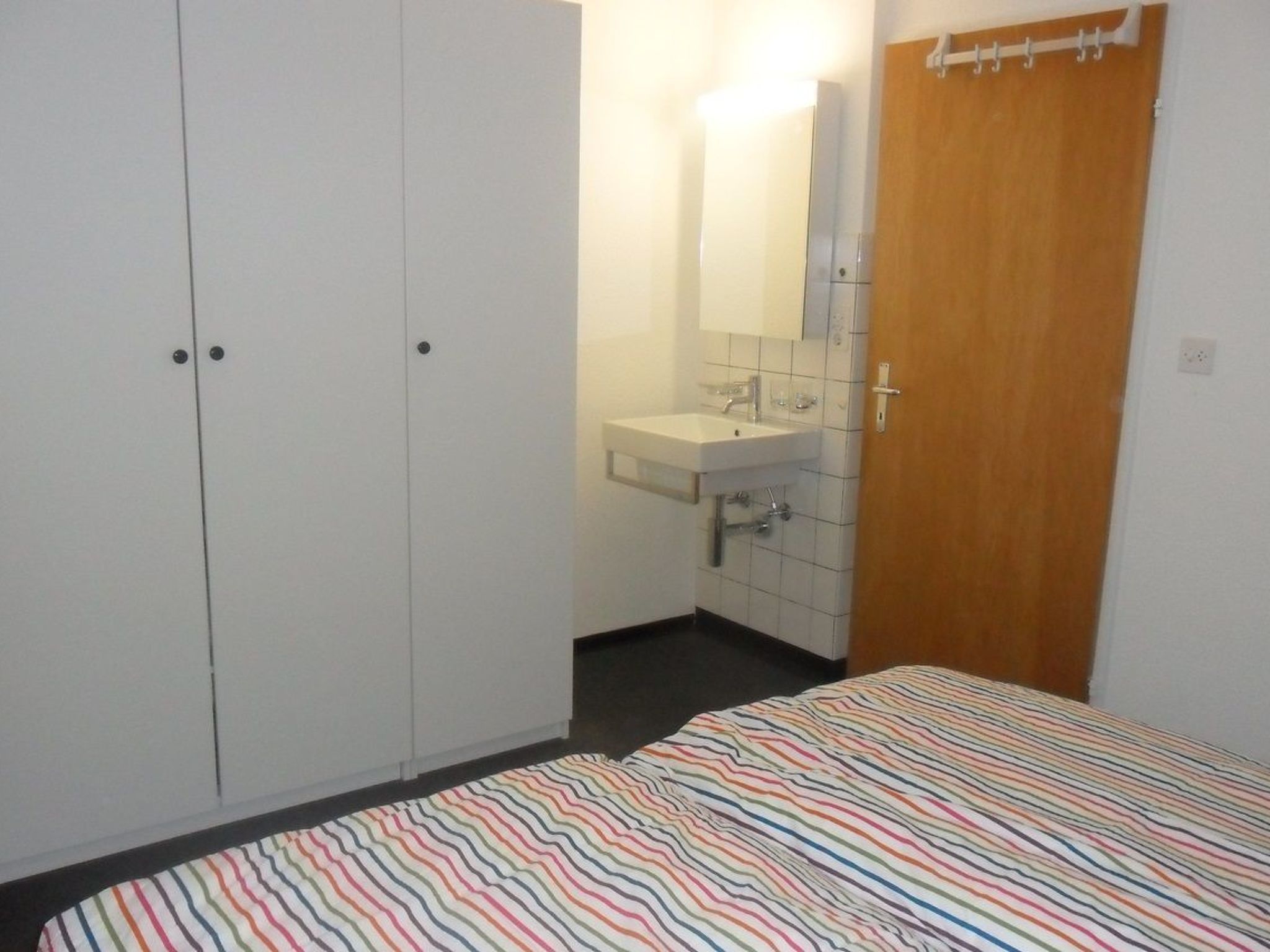 Ein Schlafzimmer mit Bett, Kleiderschrank, Badezimmer mit Waschbecken und Spiegel sowie einer Tür.