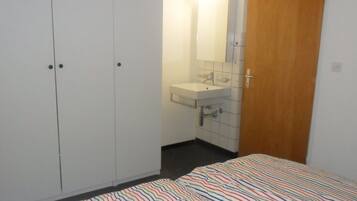 Ein Schlafzimmer mit Bett, Kleiderschrank, Badezimmer mit Waschbecken und Spiegel sowie einer Tür.