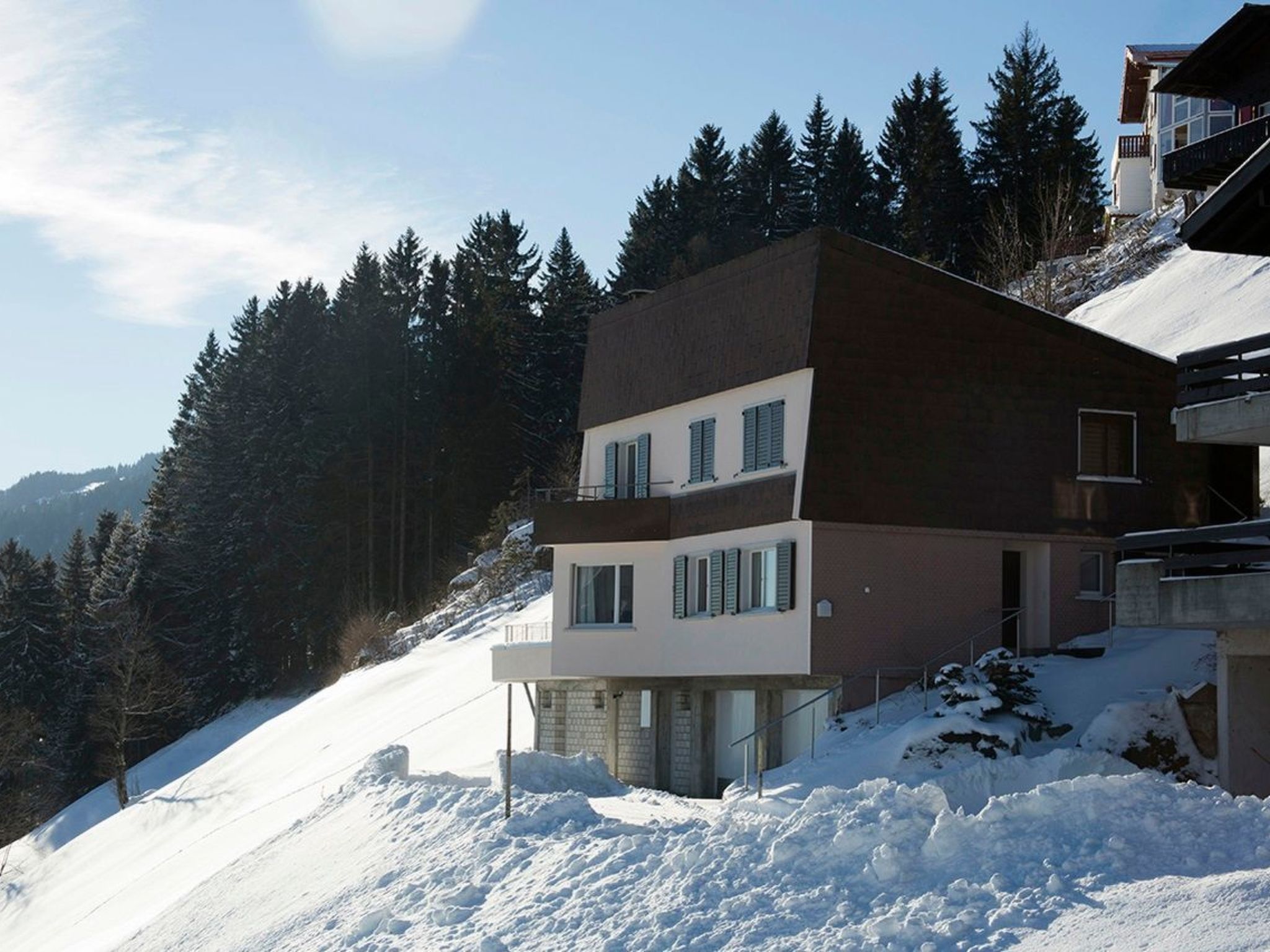 Ein mehrstöckiges Gebäude mit flachem Dach, umgeben von verschneiteter Landschaft und dichtem Wald.