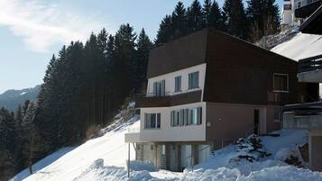 Ein mehrstöckiges Gebäude mit flachem Dach, umgeben von verschneiteter Landschaft und dichtem Wald.