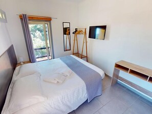 Ein Hotelzimmer mit Bett, einem Fenster mit Vorhängen, einem Spiegel, einem Fernseher und einer hölzernen Bank.