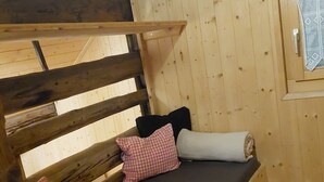 A wooden cabin interior with a bunk bed, pillows, and a window. - Chrüterhütte, (Flumserberg Tannenboden), by Interhome (Flumserberg Tannenheim)