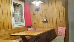 A wooden interior with a table, benches, a window with a red curtain, and a wall-mounted lantern. - Chrüterhütte, (Flumserberg Tannenboden), by Interhome (Flumserberg Tannenheim)