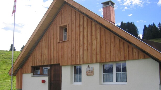 A wooden cabin with a sloped roof, a front door, a bench outside, and a sign on the wall. - Chrüterhütte, (Flumserberg Tannenboden), by Interhome (Flumserberg Tannenheim)