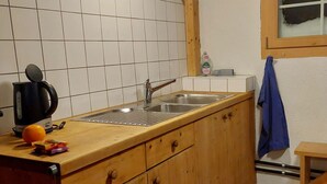 A kitchen with a sink, wooden cabinets, a kettle, and a window. - Chrüterhütte, (Flumserberg Tannenboden), by Interhome (Flumserberg Tannenheim)