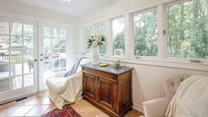 Een kamer met een houten kast, een stoel, een bed en grote ramen met uitzicht op groen.