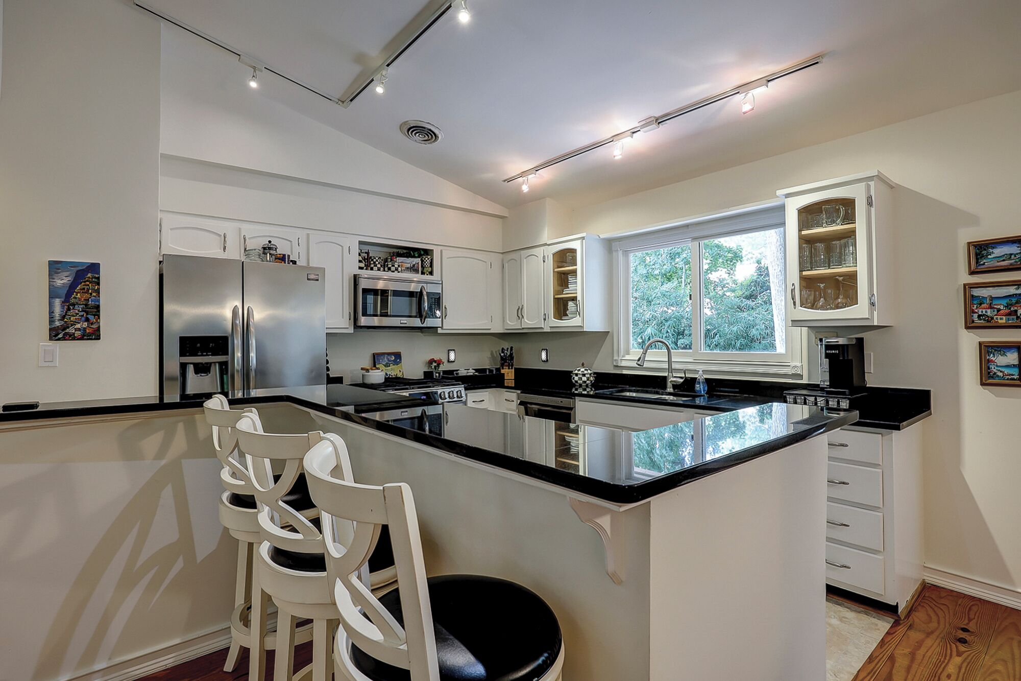 Een moderne keuken met witte kasten, roestvrijstalen apparatuur en een groot eiland met barkrukken.