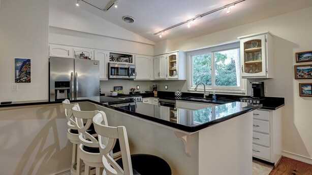 Een moderne keuken met witte kasten, roestvrijstalen apparatuur en een groot eiland met barkrukken.
