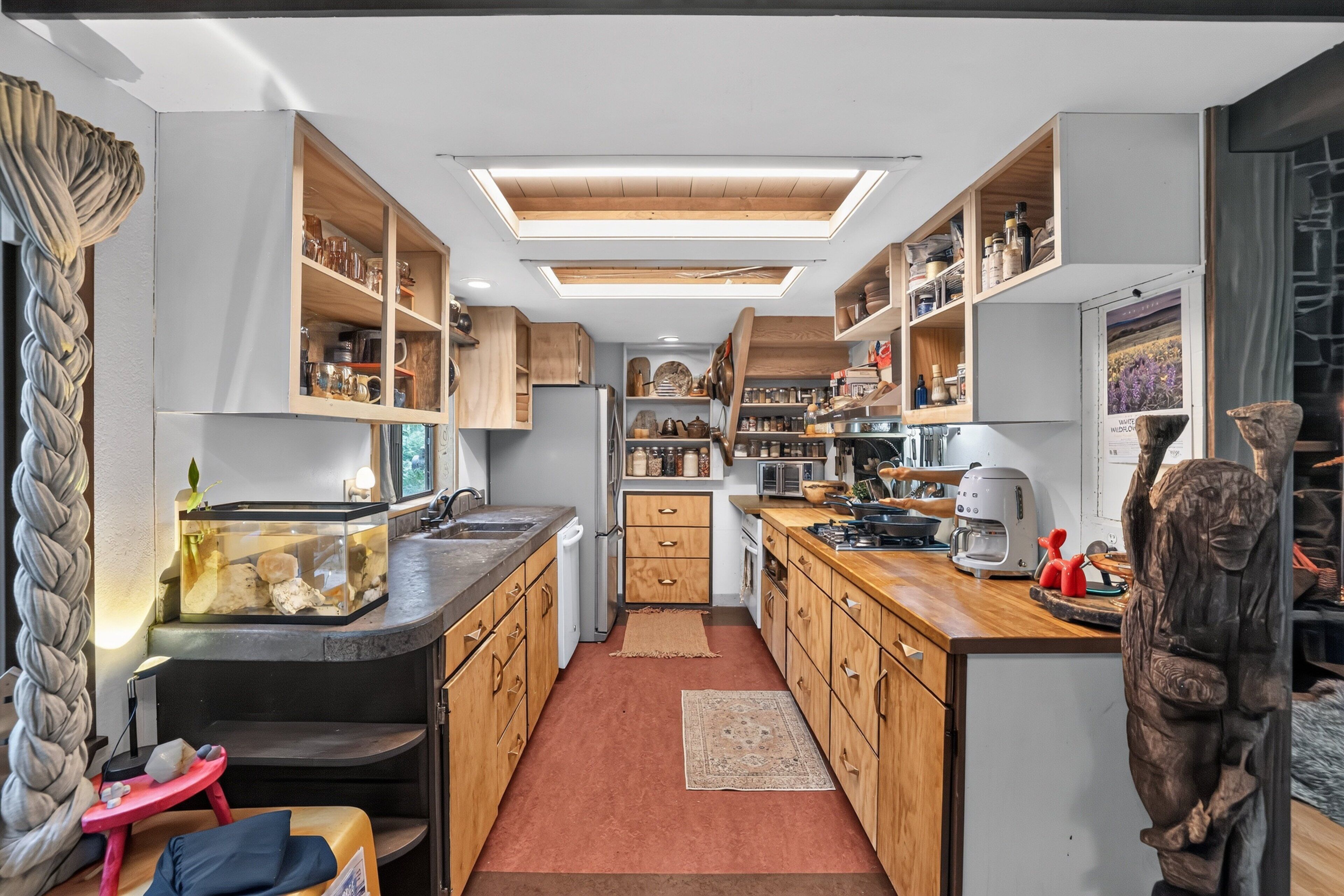 A compact kitchen with wooden cabinets, a built-in oven, and a small dining area with a red stool.