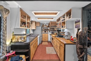 A compact kitchen with wooden cabinets, a built-in oven, and a small dining area with a red stool. - Woodland Home Near The Gorge - Private Deck 1 Bedroom Home (Washougal)