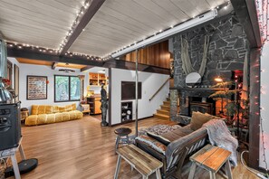 A cozy living room with a stone fireplace, wooden beams, and a staircase leading to another level. - Woodland Home Near The Gorge - Private Deck 1 Bedroom Home (Washougal)