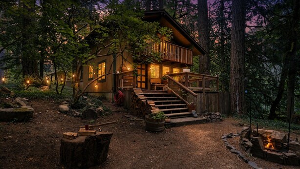A cabin with a wooden exterior, a deck, and a fire pit in a forest setting. - Woodland Home Near The Gorge - Private Deck 1 Bedroom Home (Washougal)