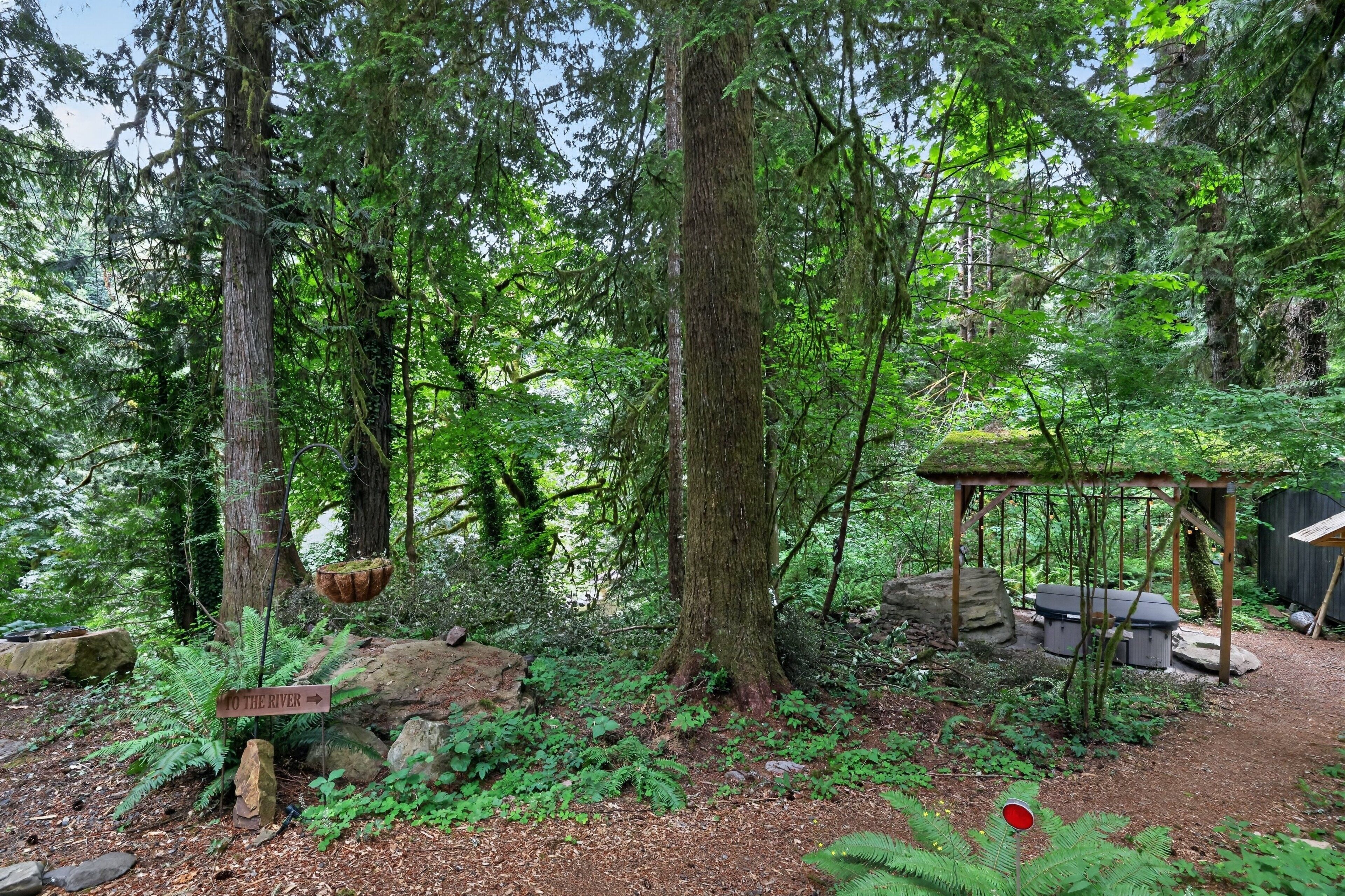 A forested area with a wooden structure, a sign pointing to the river, and a bench.