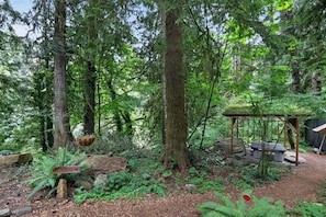 A forested area with a wooden structure, a sign pointing to the river, and a bench. - Woodland Home Near The Gorge - Private Deck 1 Bedroom Home (Washougal)
