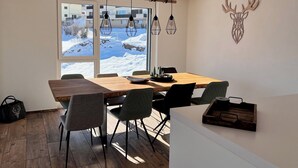 A dining area with a wooden table, chairs, pendant lights, and a view of a snowy landscape through large windows.