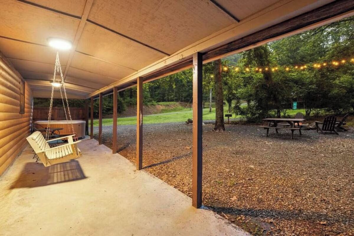 Un patio exterior cubierto con una silla colgante, una mesa de picnic y luces de cadena.