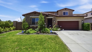 A two-story house with a stone facade, a garage, and a well-maintained lawn. - Heritage Lake Luxury Home 4 Bedroom Home (Menifee)