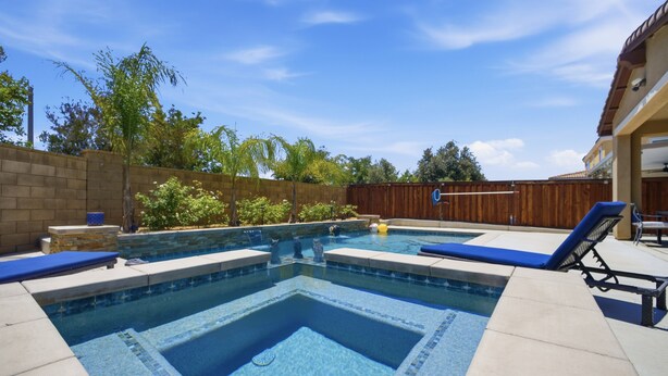A rectangular swimming pool with a tiled border, surrounded by a wooden fence, and a patio area with lounge chairs. - Heritage Lake Luxury Home 4 Bedroom Home (Menifee)
