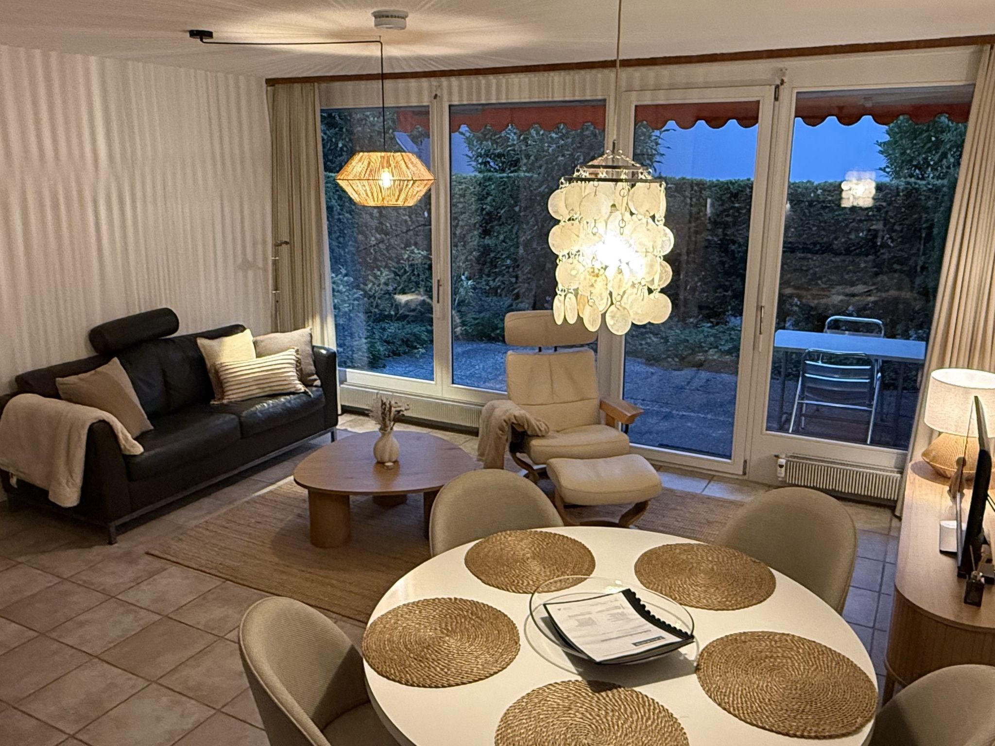 Un salon moderne comprenant un canapé, des fauteuils, une table basse et une table à manger avec des sets de table.