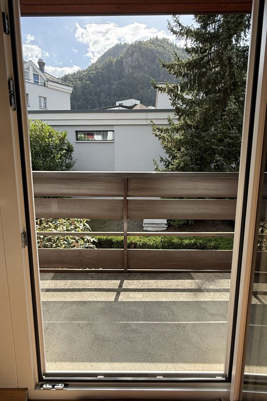 A view through a window with a wooden railing, a parking lot, and buildings in the background.