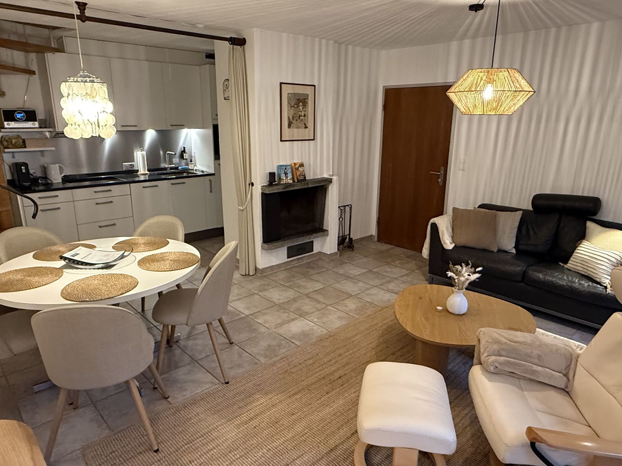 A modern living space with a dining area, a sofa set, a fireplace, and a kitchen.