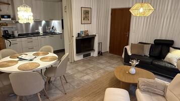 A modern living space with a dining area, a sofa set, a fireplace, and a kitchen.
