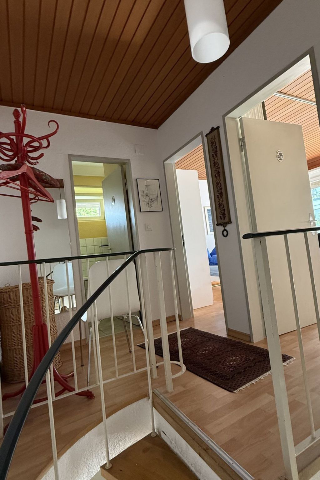Un escalier avec une rampe blanche menant à une pièce dotée d’un plafond en bois et d’une porte ornée d’un panneau décoratif.