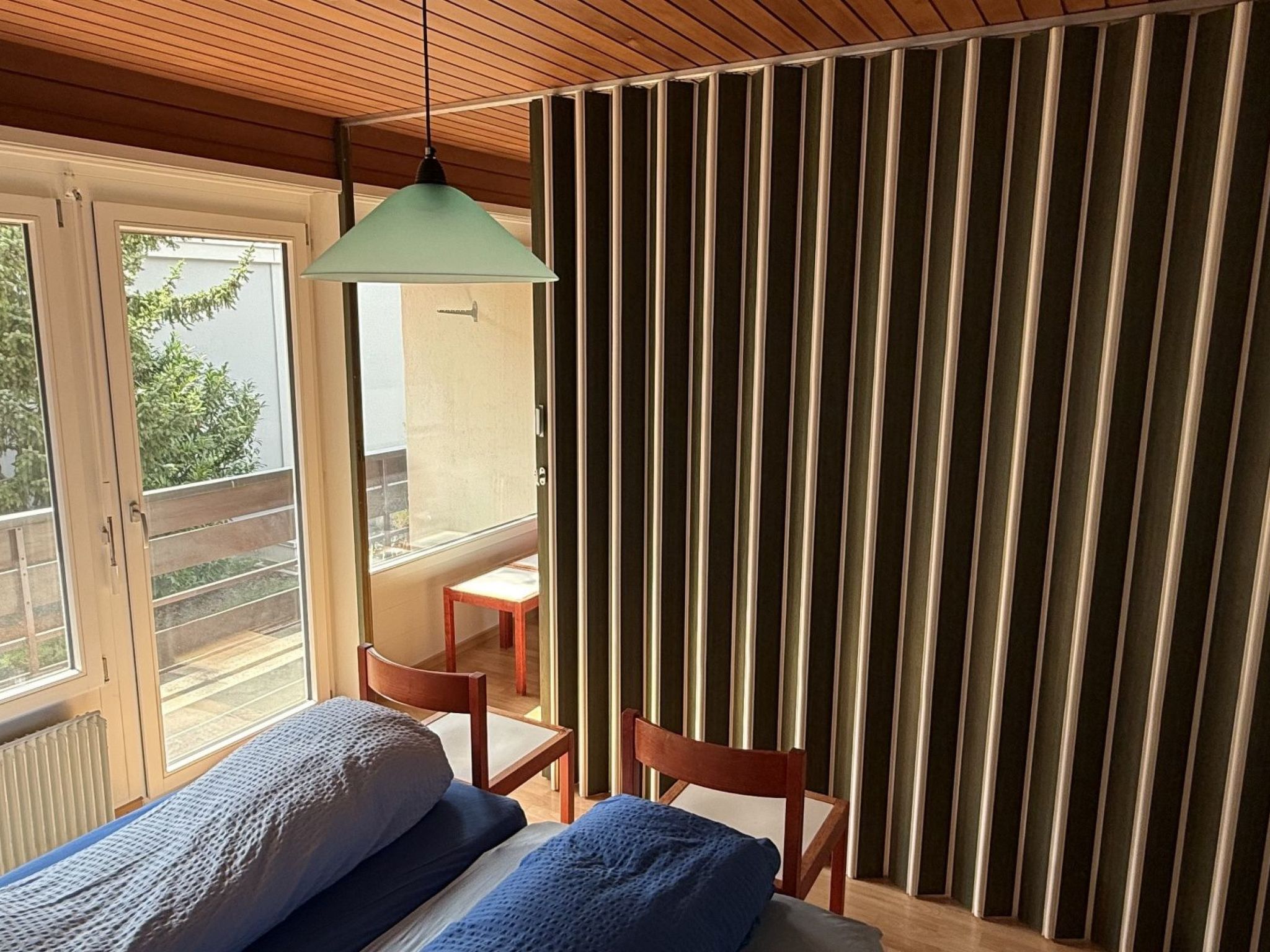 Une pièce comprenant un lit, une chaise, une table et donnant sur l’extérieur.