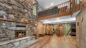Une pièce spacieuse avec une cheminée en pierre, un plancher en bois, une mezzanine avec une rambarde en bois et un escalier.
