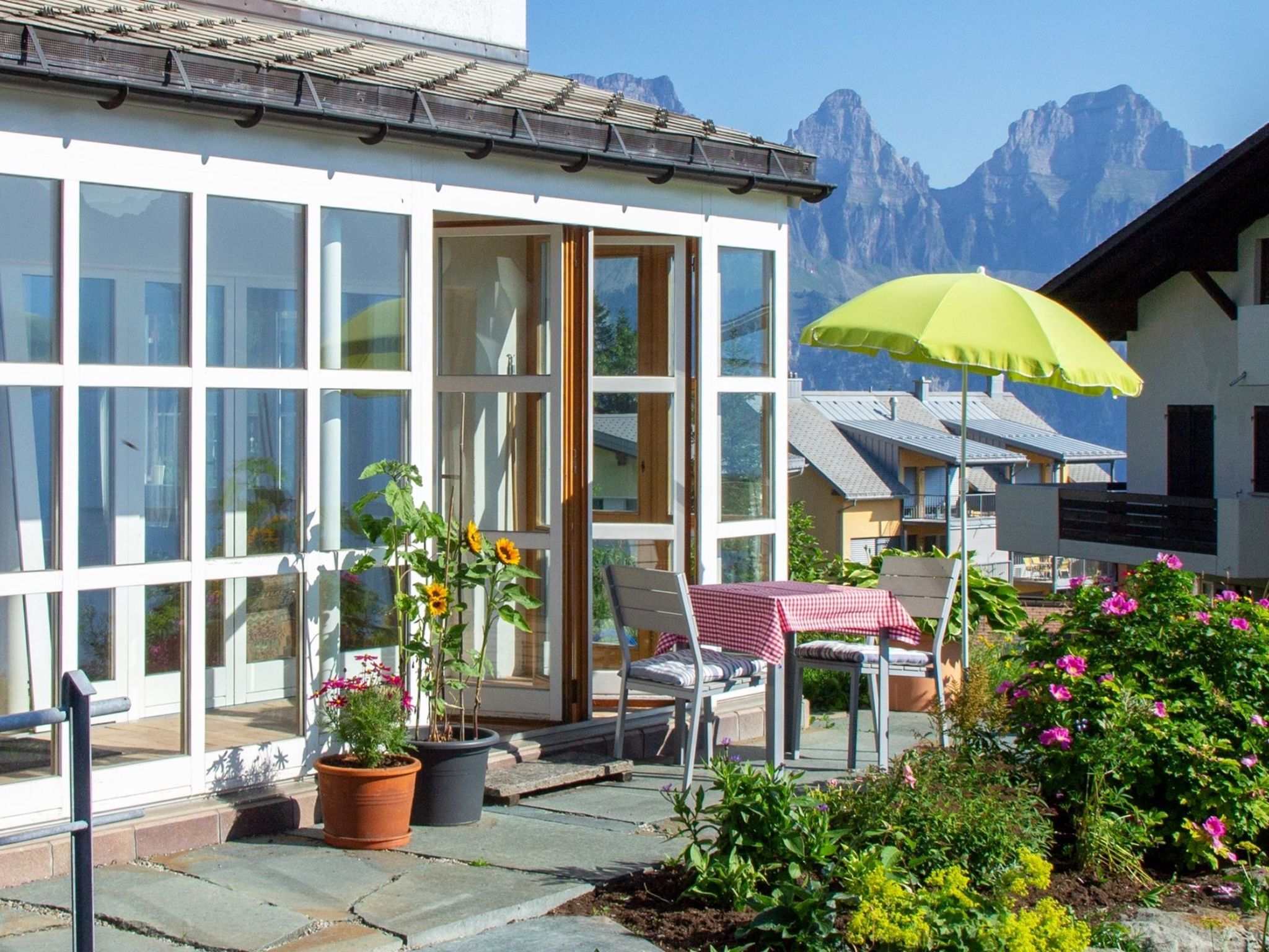 A hotel with large windows, a patio with a table and chairs, and a mountain view.