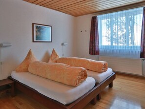Ein Zimmer mit Holzboden, einem Bett mit Kissen, einem Bild an der Wand und einem Fenster mit Vorhängen.