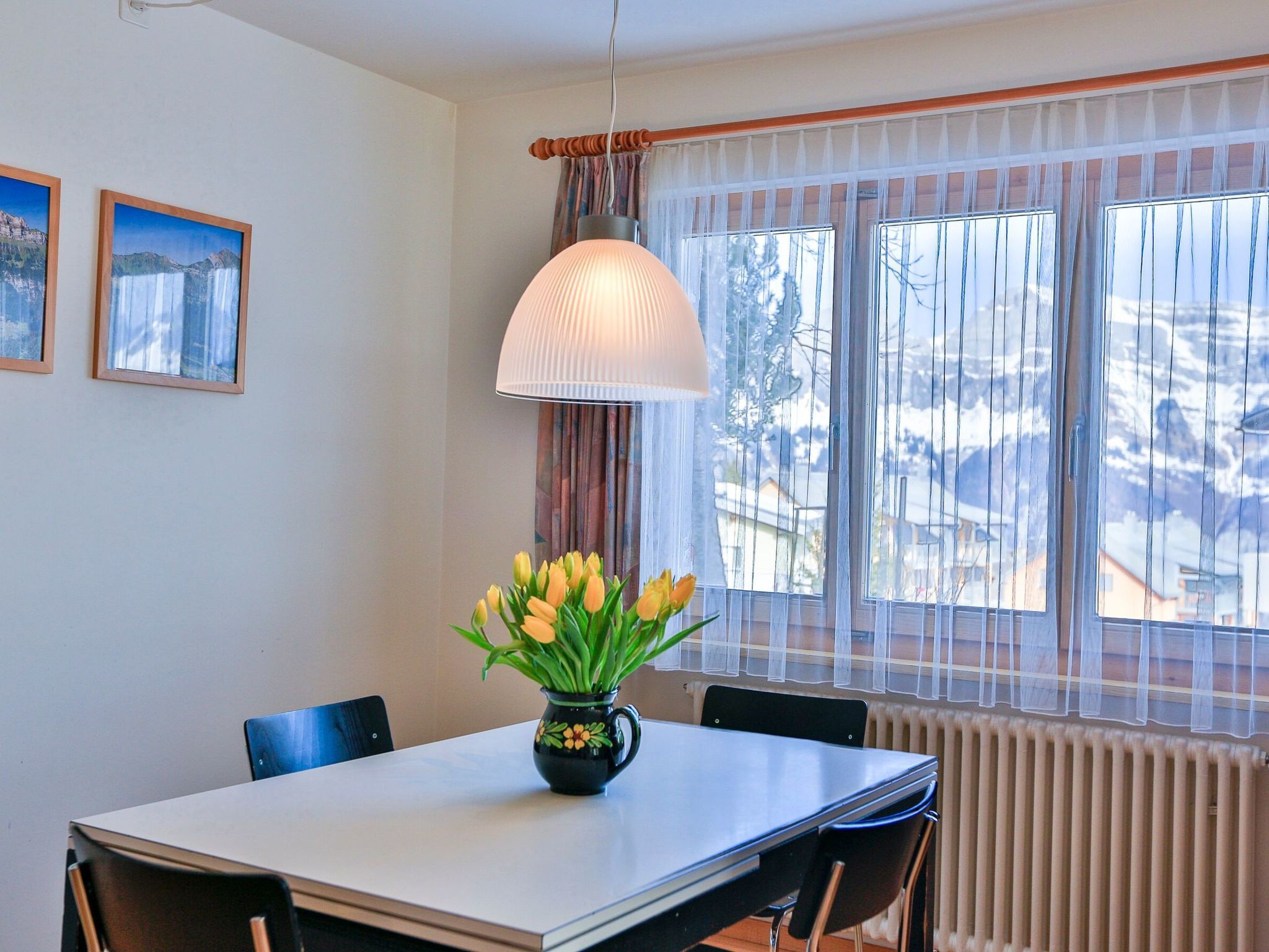 Ein Essbereich mit Tisch, Stühlen, einer Blumenvase und einem Fenster mit Vorhängen.
