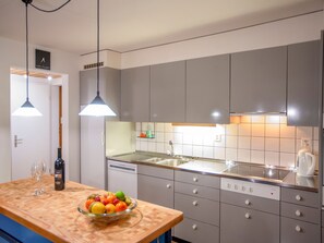 A modern kitchen with grey cabinets, a wooden countertop, a bowl of fruit, and a wine bottle. - Steinröschen, (Flumserberg Tannenboden), by Interhome (Flumserberg Tannenheim)