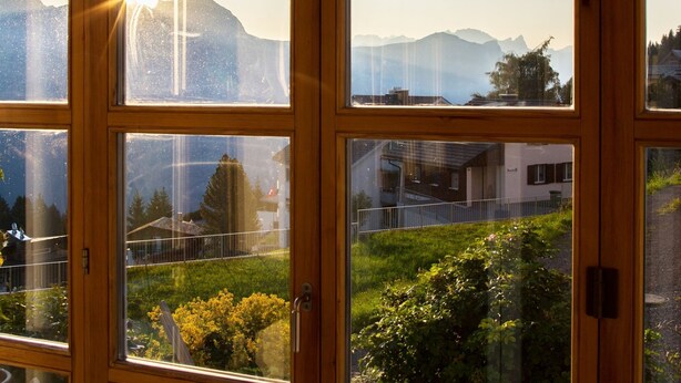 A view through a window with multiple panes, revealing a mountainous landscape and a residential area with houses and greenery. - Steinröschen, (Flumserberg Tannenboden), by Interhome (Flumserberg Tannenheim)