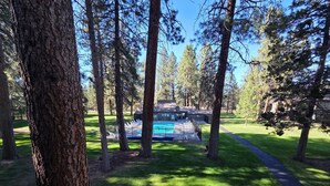 Une piscine entourée de grands arbres, un bâtiment doté d’une terrasse couverte et une pelouse bien entretenue.