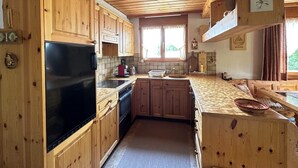 A wooden cabin-style kitchen with a refrigerator, stove, and wooden cabinets.