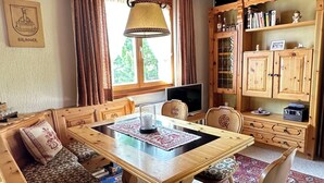 A cozy room with a wooden dining table, bench seating, a television, wooden cabinets, and a window with curtains.