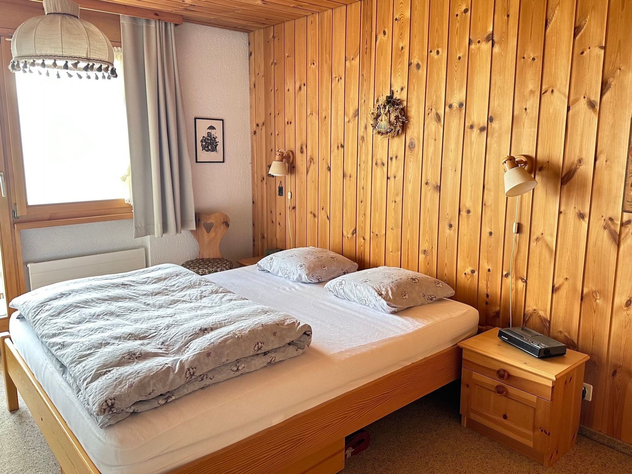 Una habitación con paneles de madera, una cama, una mesita de noche, una lámpara y un cuadro en la pared.