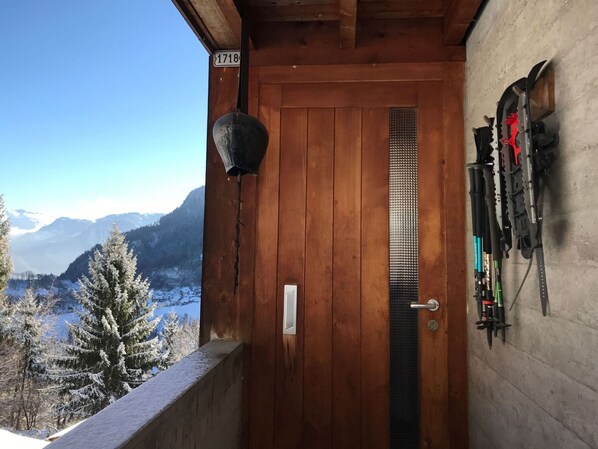 A wooden door with a number plate, a metal handle, and a view of snow-covered mountains.